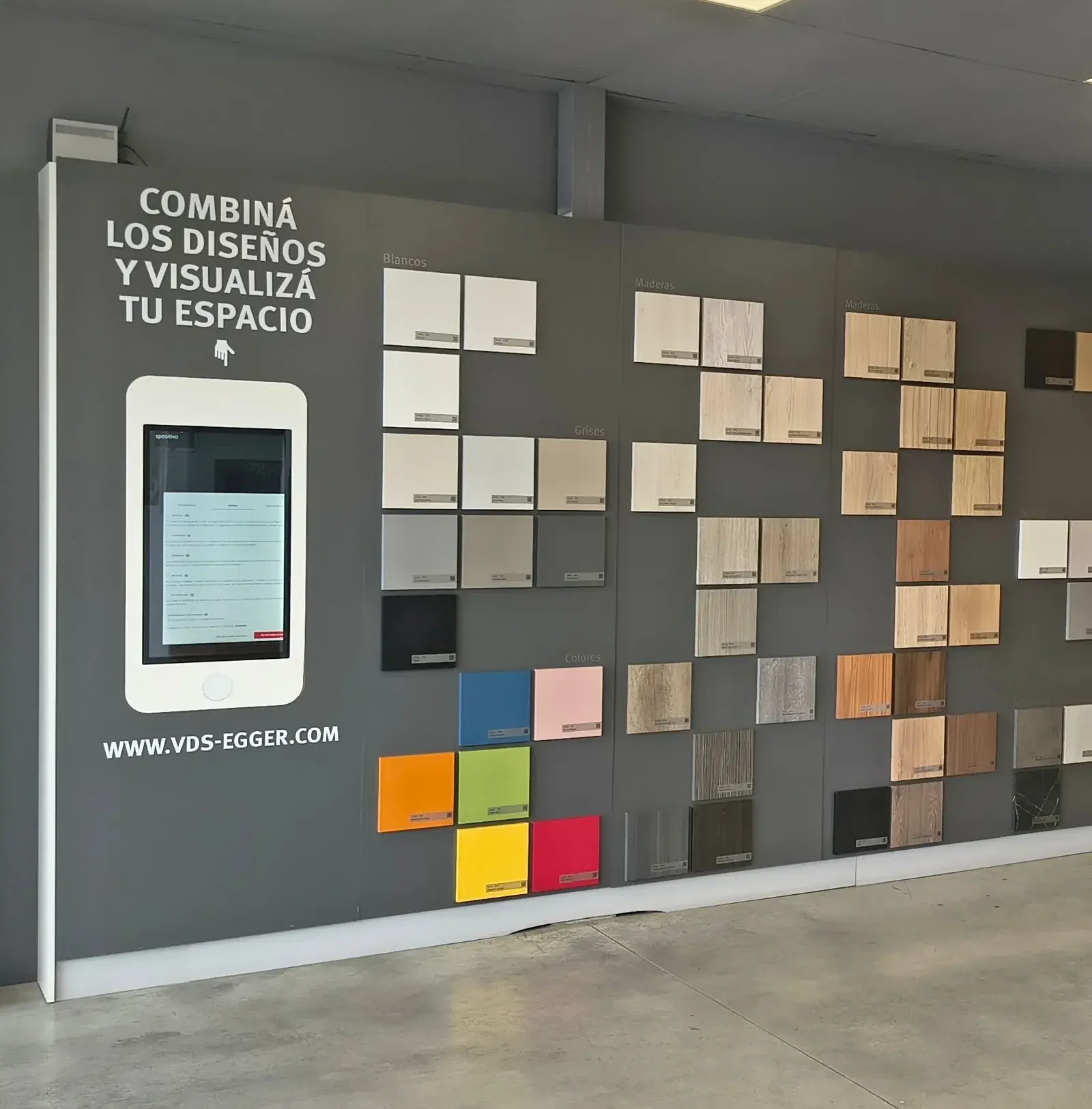 Pared del showroom con las muestras de placas ordenadas por familia —blancos, unicolores, maderas— y una pantalla táctil del Estudio de Diseño Virtual.